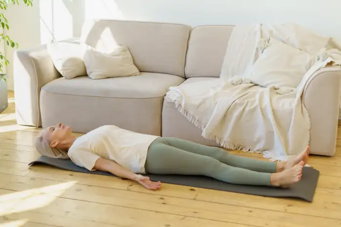 Frau praktiziert eine liegende Meditation zuhause im Wohnzimmer mit dem Achtsamkeitskurs online