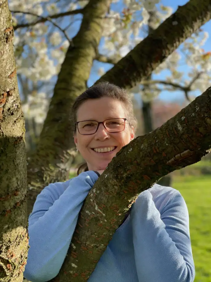 Achtsamkeitslehrerin Patricia Haurand lehnt an einem Baum und strahlt Freude aus. Achtsamkeit Online-Kurs.